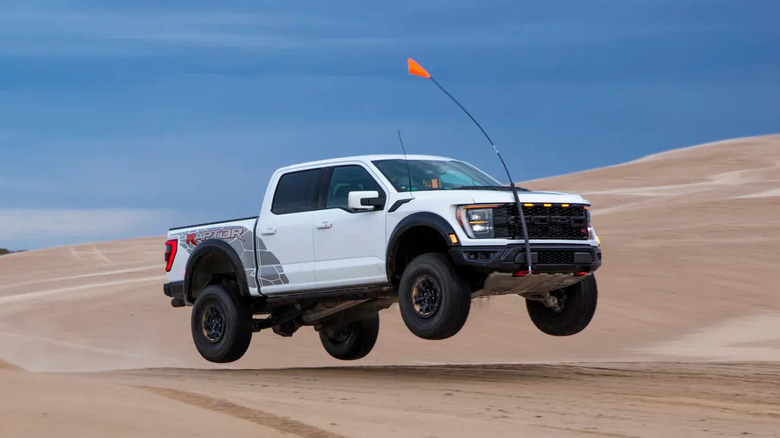 A white Ford F-150 Raptor jumping over a sand dune