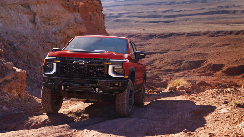 A red 2027 Chevrolet Silverado 1500 ZR2 Bison climbing a mesa platform in the desert.
