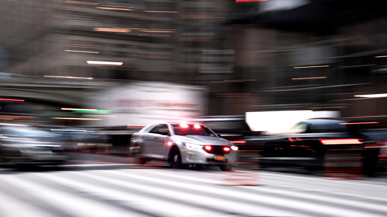 An image with substantial motion blur showing an NYPD Ford Taurus driving on city streets with its emergency lights illuminated.