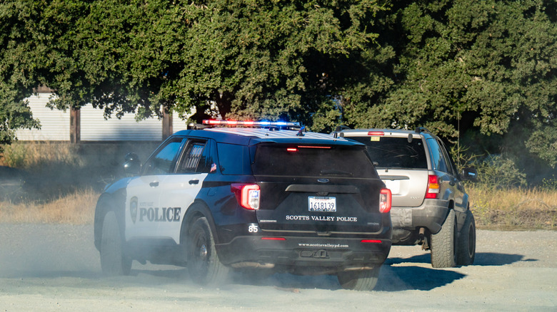 A Ford Police Interceptor SUV kicks up dust chasing a Jeep Grand Cherokee