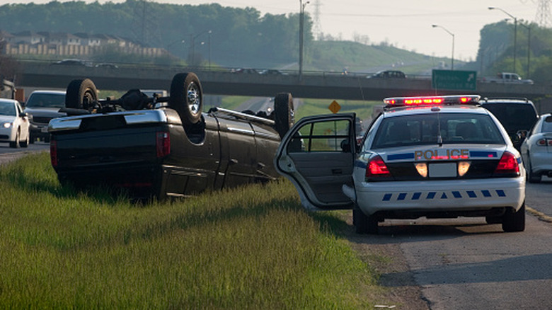 A police car on the side of the highway next to an SUV that rolled over at a high rate of speed.