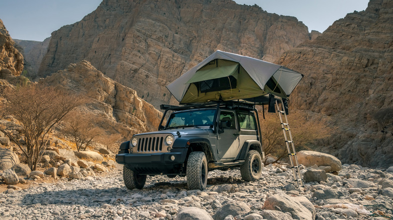 A Jeep Wrangler parked in the desert with a rooftop tent deployed.