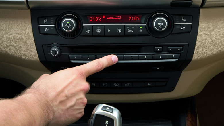 A finger points at the fourth of eight buttons on the center dashboard console of a BMW M5.