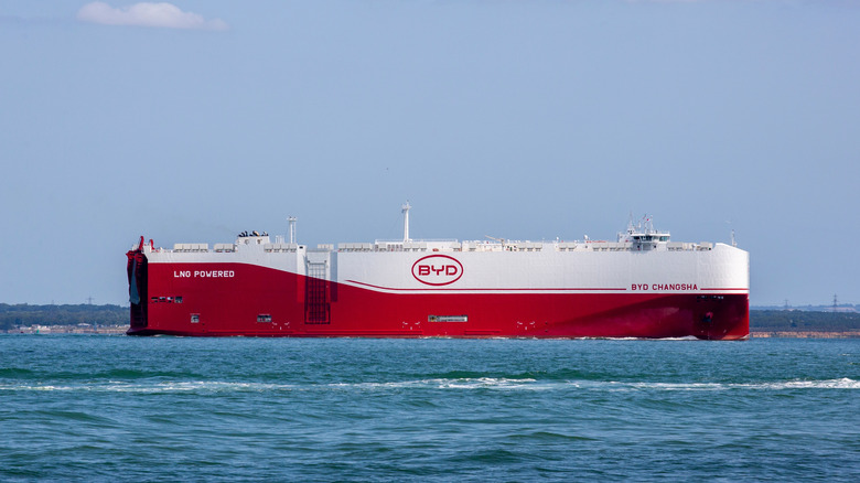 A red and white BYD car carrier boat leaving a port.