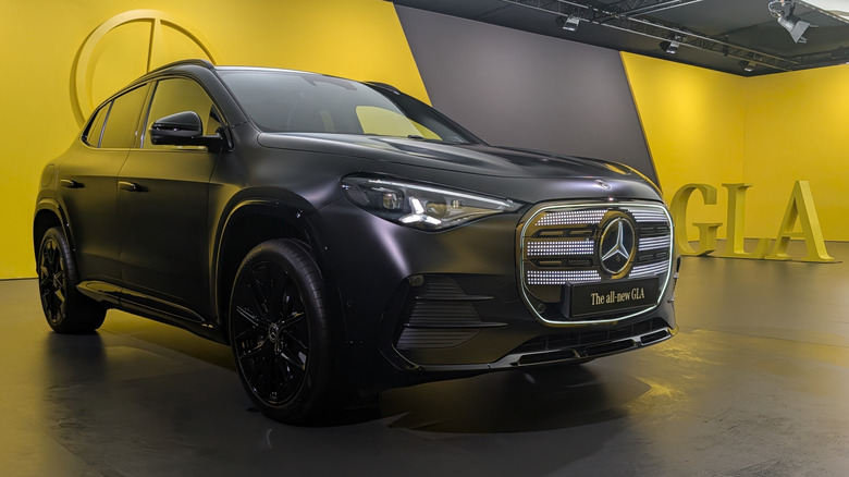 A matte black 2028 Mercedes-Benz GLA parked in a staging area surrounded by yellow walls
