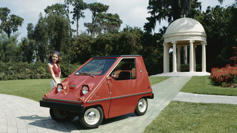A period photograph of a bright-red CitiCar from the 1970s in a city park