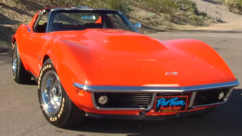 A bright orange C3 Corvette L88 coupe with its iconic high-clearance hood scoop, chrome front bumper, and vintage white-lettered tires, parked on an open lot.
