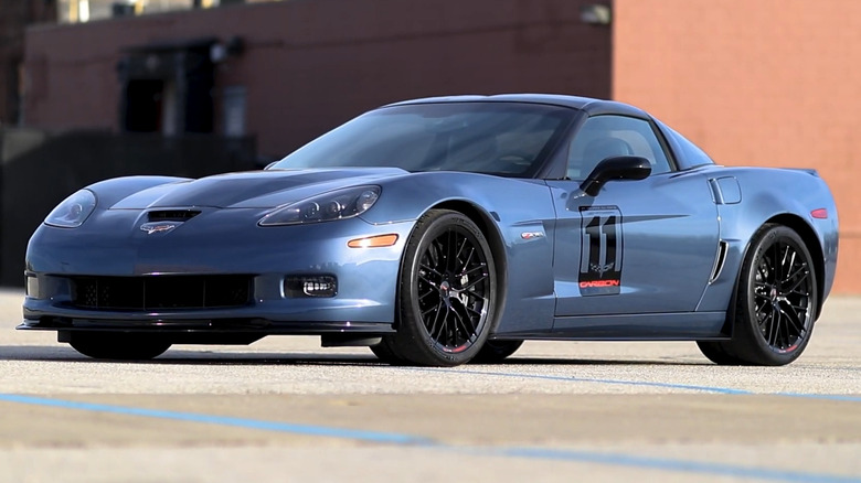 A Supersonic Blue 2011 C6 Corvette Z06 Carbon Limited Edition with black wheels and a carbon-fiber splitter, parked on an open concrete lot with a custom "11 Carbon" door decal.
