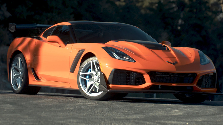 An orange C7 Corvette ZR1 equipped with the high-downforce ZTK rear wing, carbon fiber splitter, and blue brake calipers, parked on a mountain road.