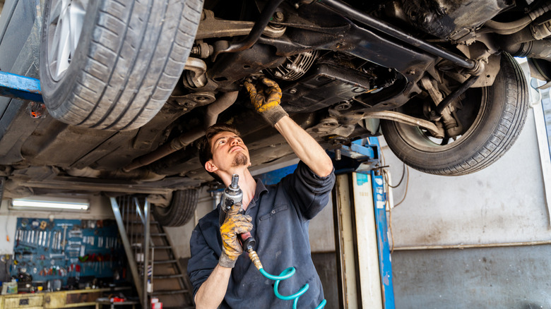 A mechanic underneath a car on a lift.