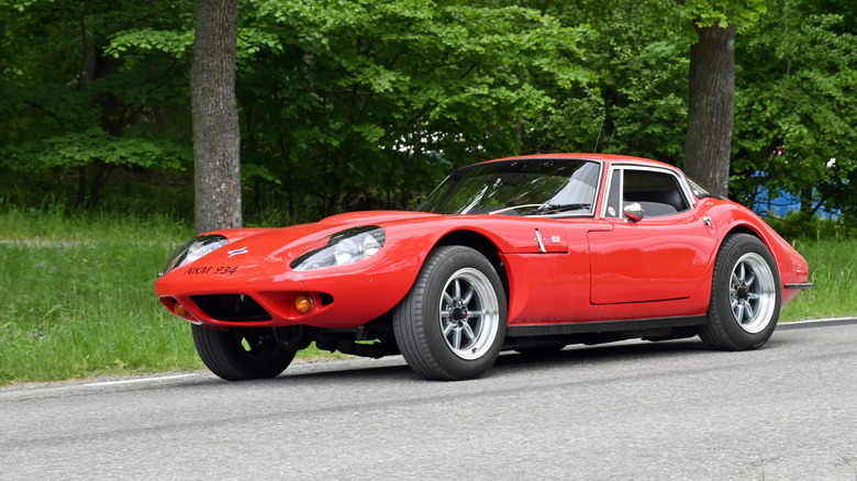 Red 1971 Marcos parked on the side of a road with trees in the background.