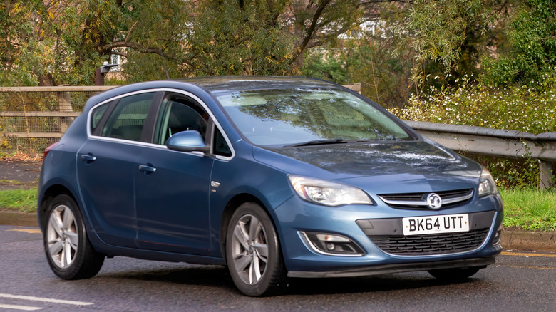 Blue Vauxhall Astra driven down a road with trees in background.
