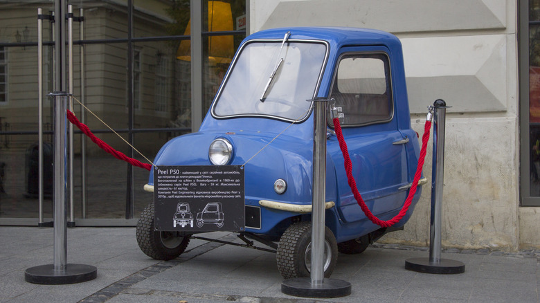 Blue Peel P50 displayed outdoors behind a red rope stanchion.