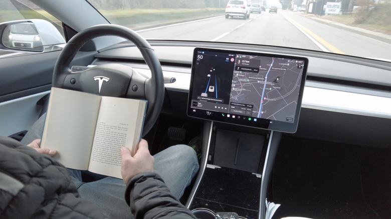 Person reading a book while behind the wheel of a Tesla