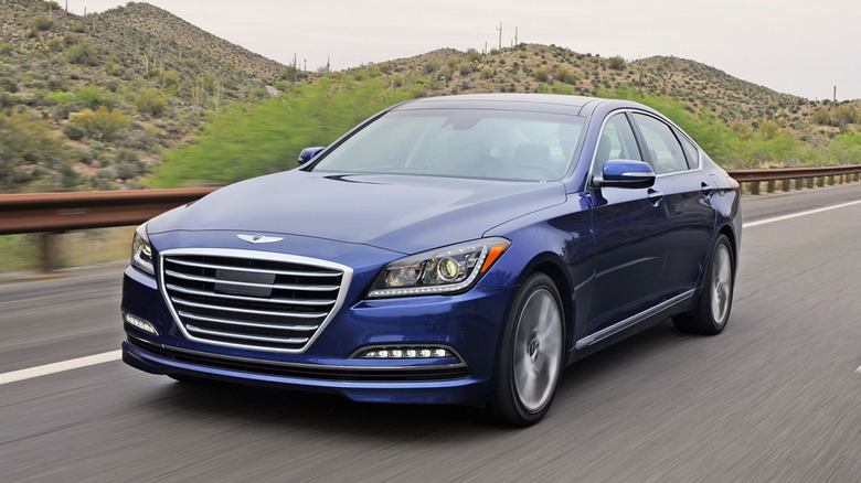 A blue 2015 Hyundai Genesis driving on a road by hills