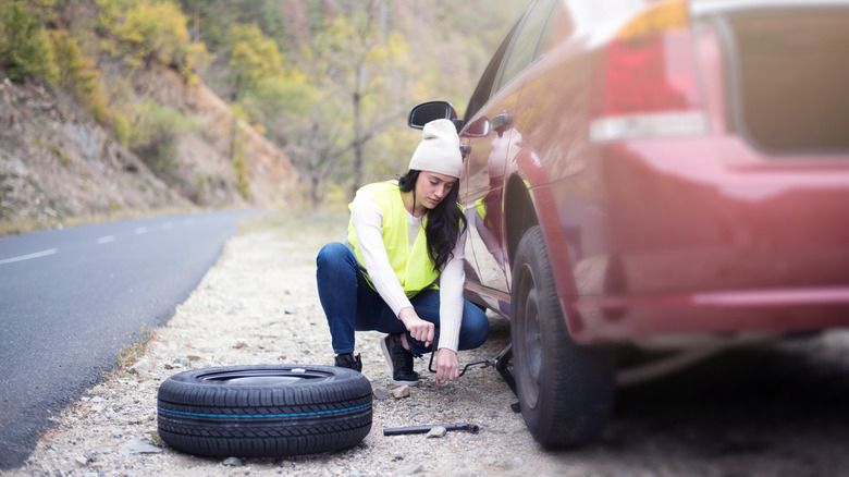 A women changes a car tire on the shoulder of a road.