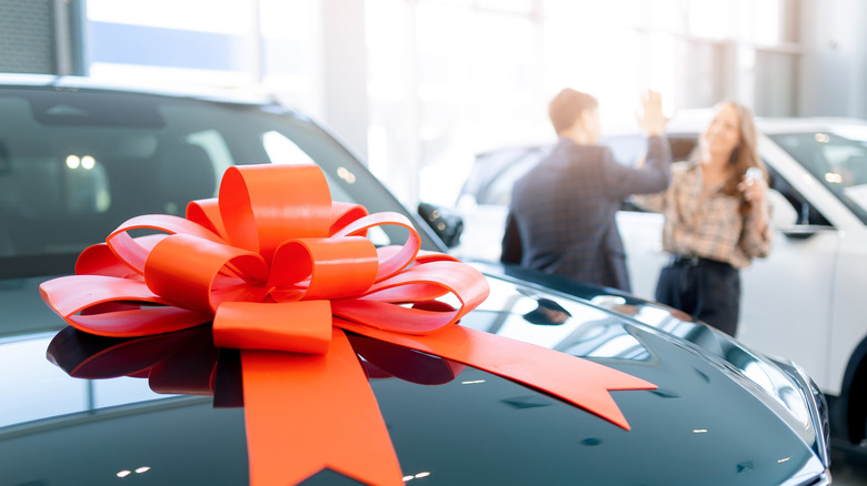 A man and a woman give a high five in the background of a dealership where a new car model wears a red bow.