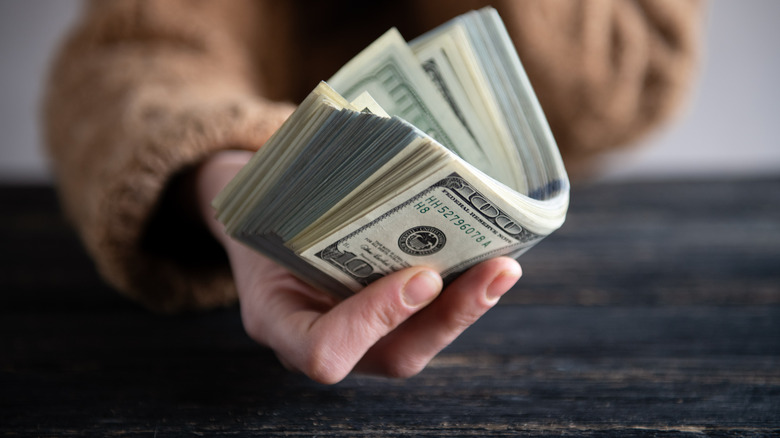 A hand extends a stack of cash.