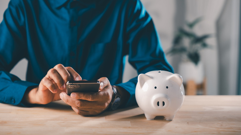A man uses his phone near a piggy bank.