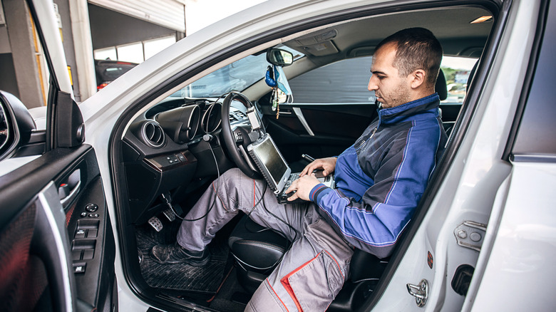 A mechanic running diagnostics in a car with a laptop.